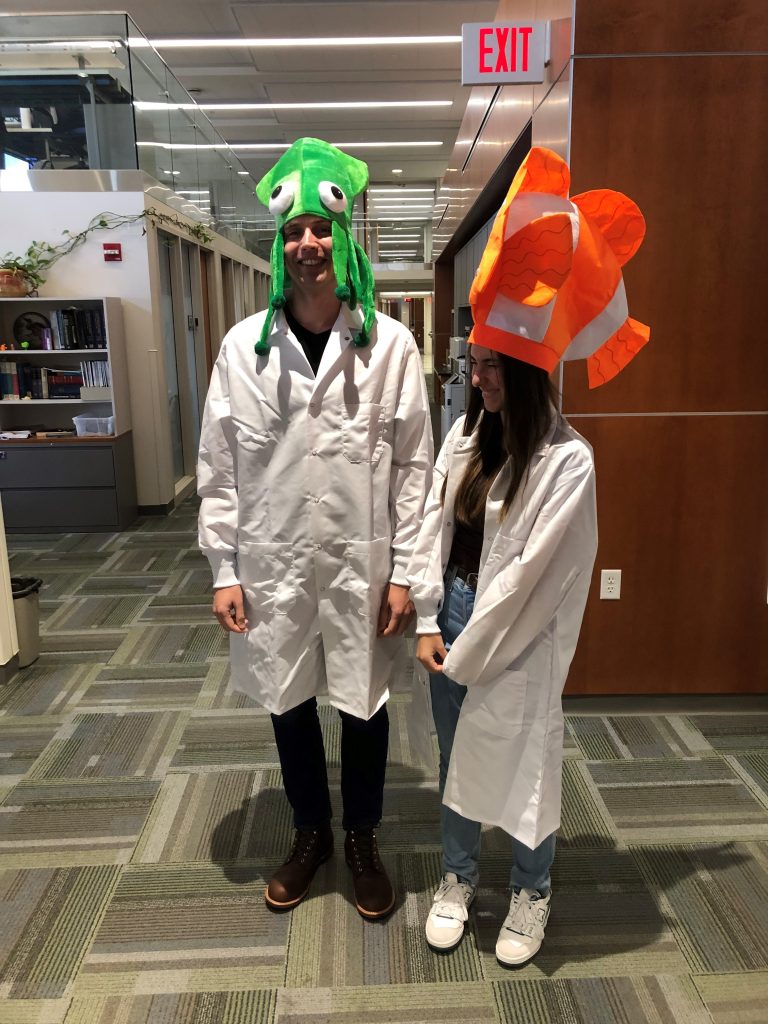 Two students in lab coats wearing colorful fish hats for a Halloween party. 