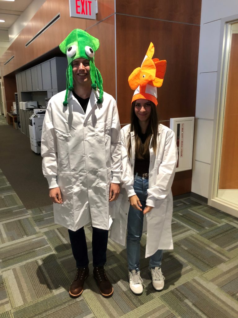 Two students in lab coats wearing colorful fish hats for a Halloween party. 