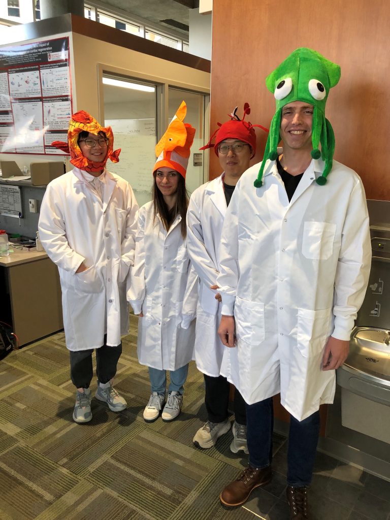 Four students in lab coats wearing colorful fish hats for a Halloween party. 