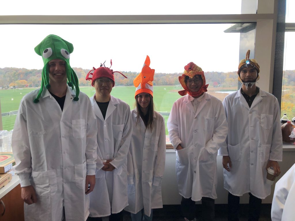 Four students in lab coats wearing colorful fish hats for a Halloween party. 