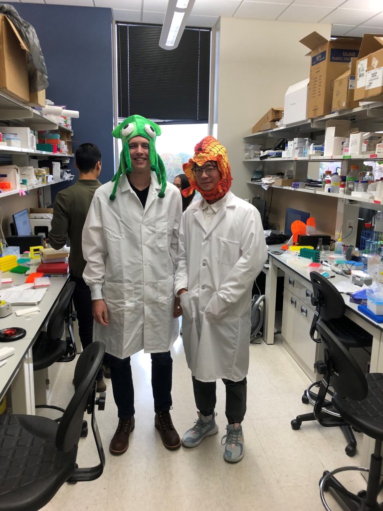 Two students in lab coats wearing colorful fish hats for a Halloween party. 