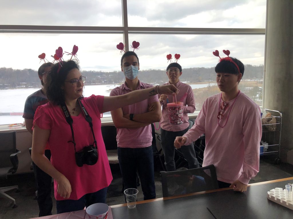 Four people in pink shirts looking at a jar of candy for a Valentine's Day party. 